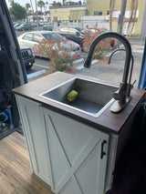 Modern kitchen setup in an rv rental camper van, with a stainless steel sink, wood counter, and white cabinet.