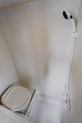 Compact white bathroom in an RV rental, featuring a space-saving toilet and handheld shower. Efficient design for travel.