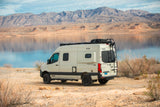 Scenic RV rental adventure: A cream-colored van by a tranquil lake with mountains reflecting, perfect for outdoor travel.