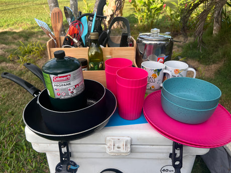 RV rental ready! Essential camping cooking gear, including propane, pots, utensils, and dinnerware, all set on a cooler for outdoor adventures.