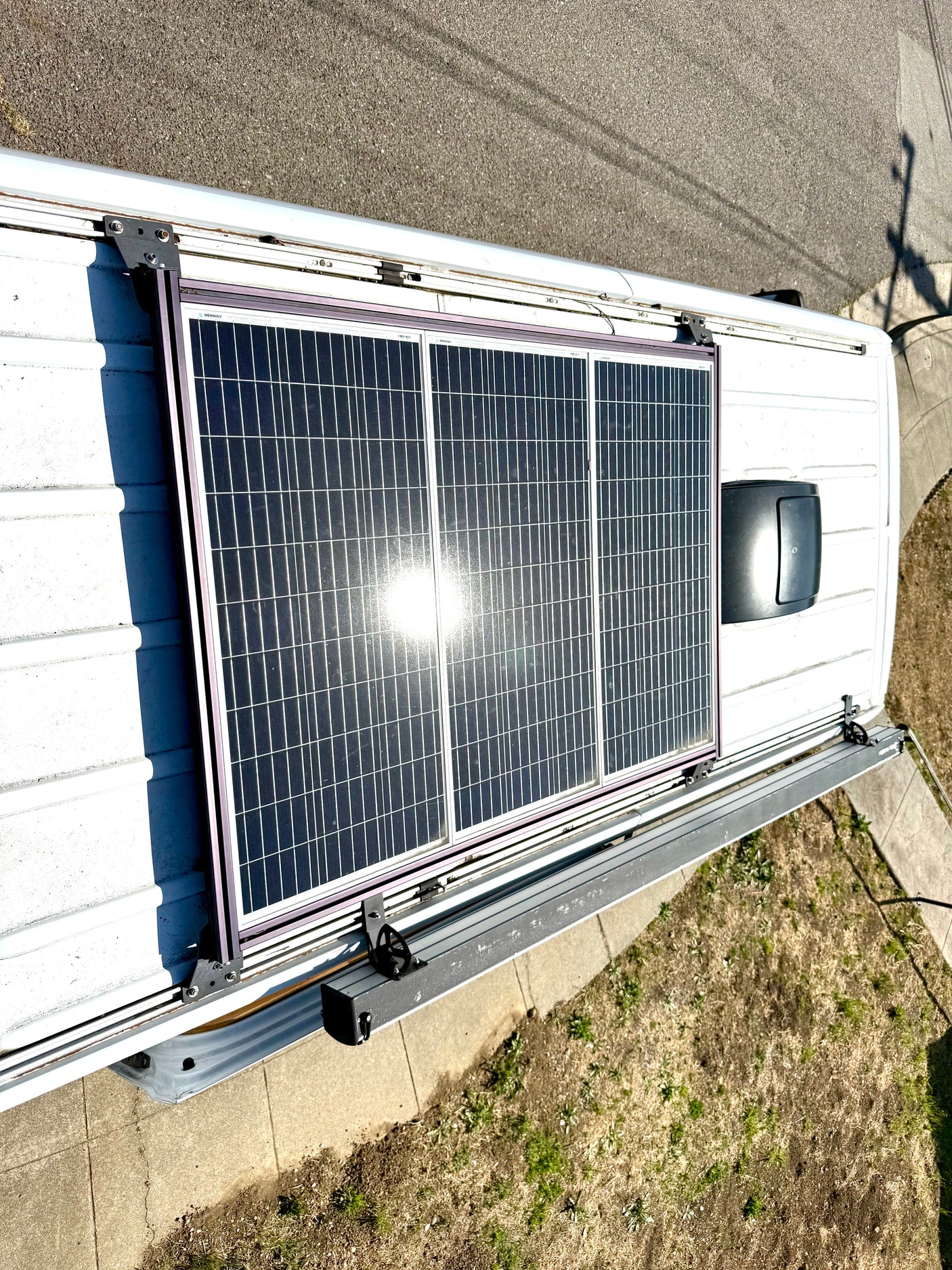 Overhead view of a white camper van / RV rental with three Renogy solar panels providing off-grid power, alongside an awning track.