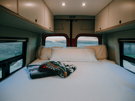 Inside an RV rental: a spacious bedroom area with a large bed, crisp white bedding, and decorative blankets.
