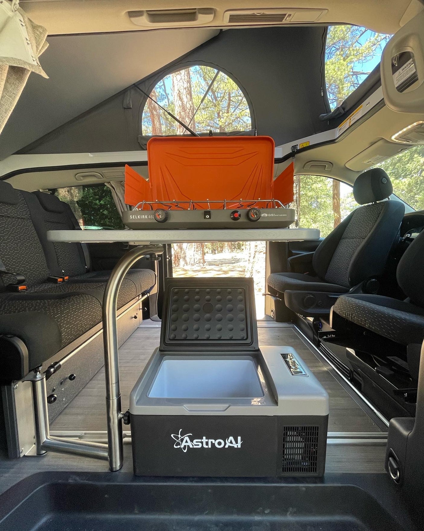 Inside an RV rental pop-top van: GSI stove, AstroAI cooler, & convertible seating for outdoor cooking & camping.