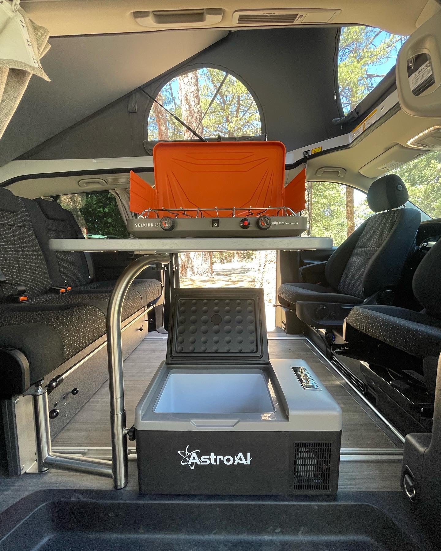 Inside an RV rental pop-top van: GSI stove, AstroAI cooler, & convertible seating for outdoor cooking & camping.