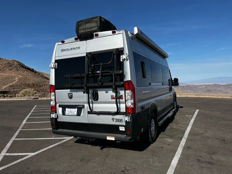 Silver Thor Sequence rv rental, with bike rack, parked at a desert mountain viewpoint under clear blue skies.