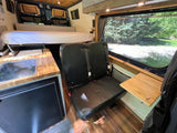 RV rental: See a camper van's interior with a rear bed, kitchen, two passenger seats, and a large side window.