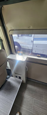 Inside an RV rental: a window with a view, modern cabinet with a pull-out table, power outlets, and cozy seating.