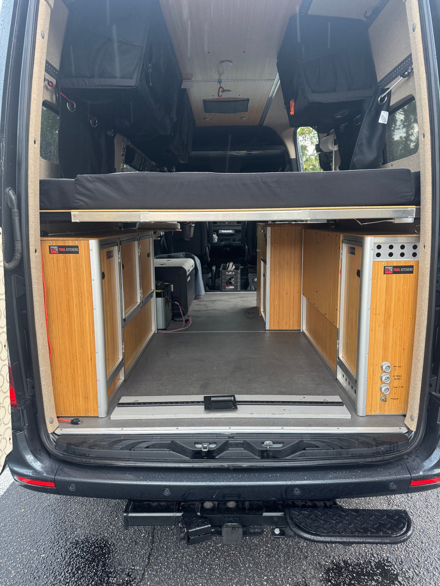 RV rental camper van interior: rear view showcasing a raised bed, modular Trail Kitchens cabinets, and overhead storage.