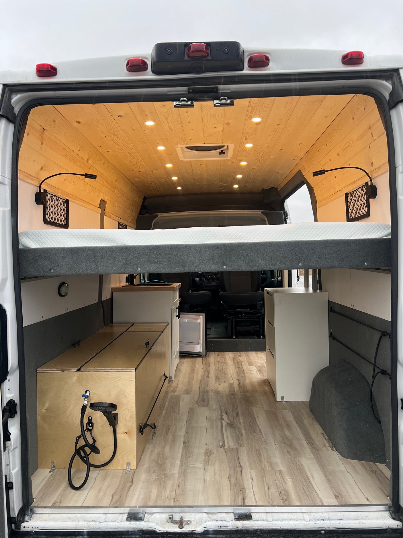 This RV rental's spacious camper van interior showcases a raised bed, custom kitchen unit, and clever storage solutions.