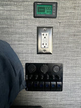 RV rental tech: Battery monitor, GFCI outlet, and Nilight 12V panel with USB/switches on textured wall.
