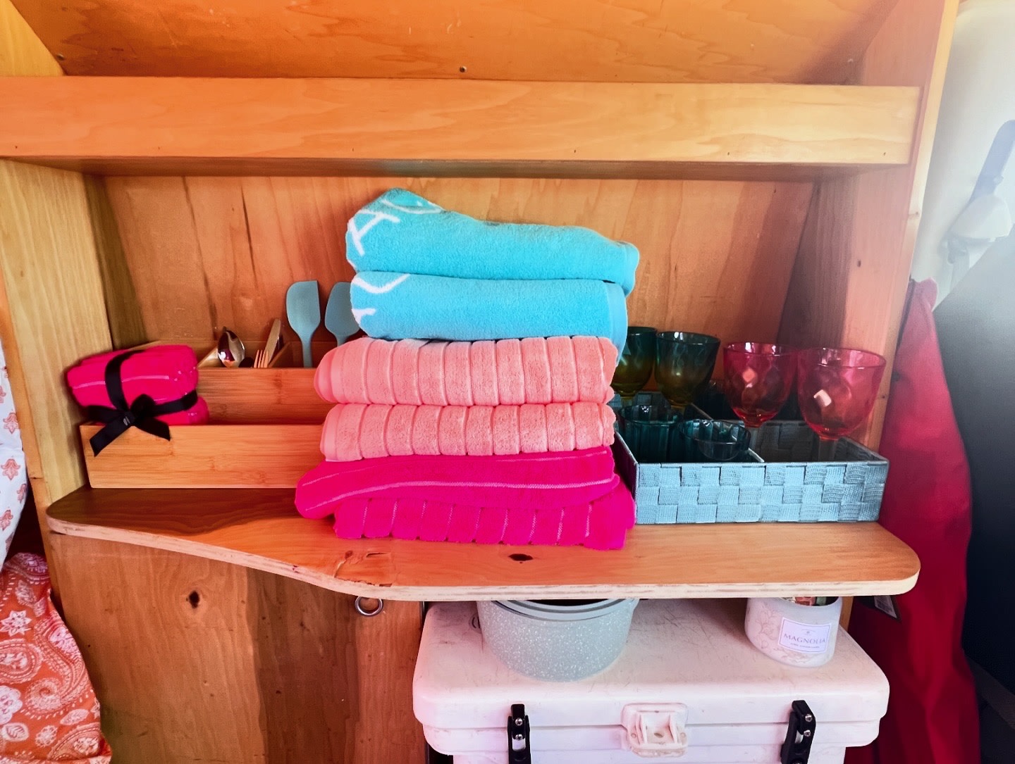 Thoughtful RV rental amenities: vibrant towels, utensils, & glassware neatly arranged in wooden shelving.