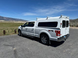 White Ford F-150 pickup with utility camper shell parked in a scenic landscape, great for an rv rental adventure.