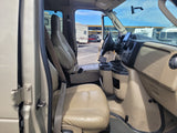 Inside a Ford E-Series RV rental. Driver's cockpit with steering wheel, dashboard screen, and passenger seat visible. RVs are outside.