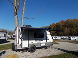 A 'SPORTSMEN Classic' travel trailer with awning extended in an RV rental lot, with other campers and autumn trees under a blue sky.