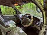 Inside an RV rental: driver's area with custom steering wheel, dashboard, and lush forest view. Perfect for nature adventures.