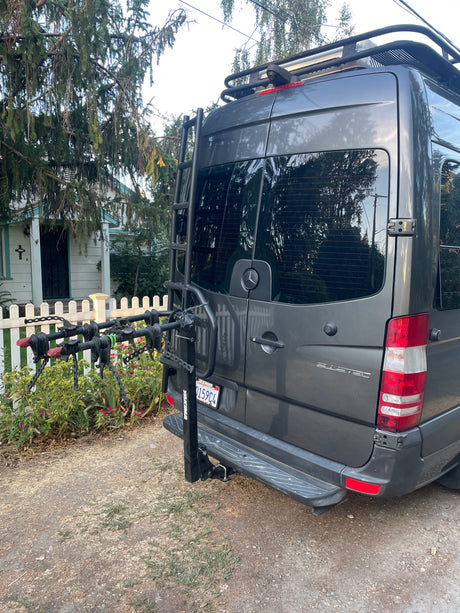 Rear view of a grey Mercedes Sprinter rv rental van, equipped with a ladder, roof rack, and bike rack.