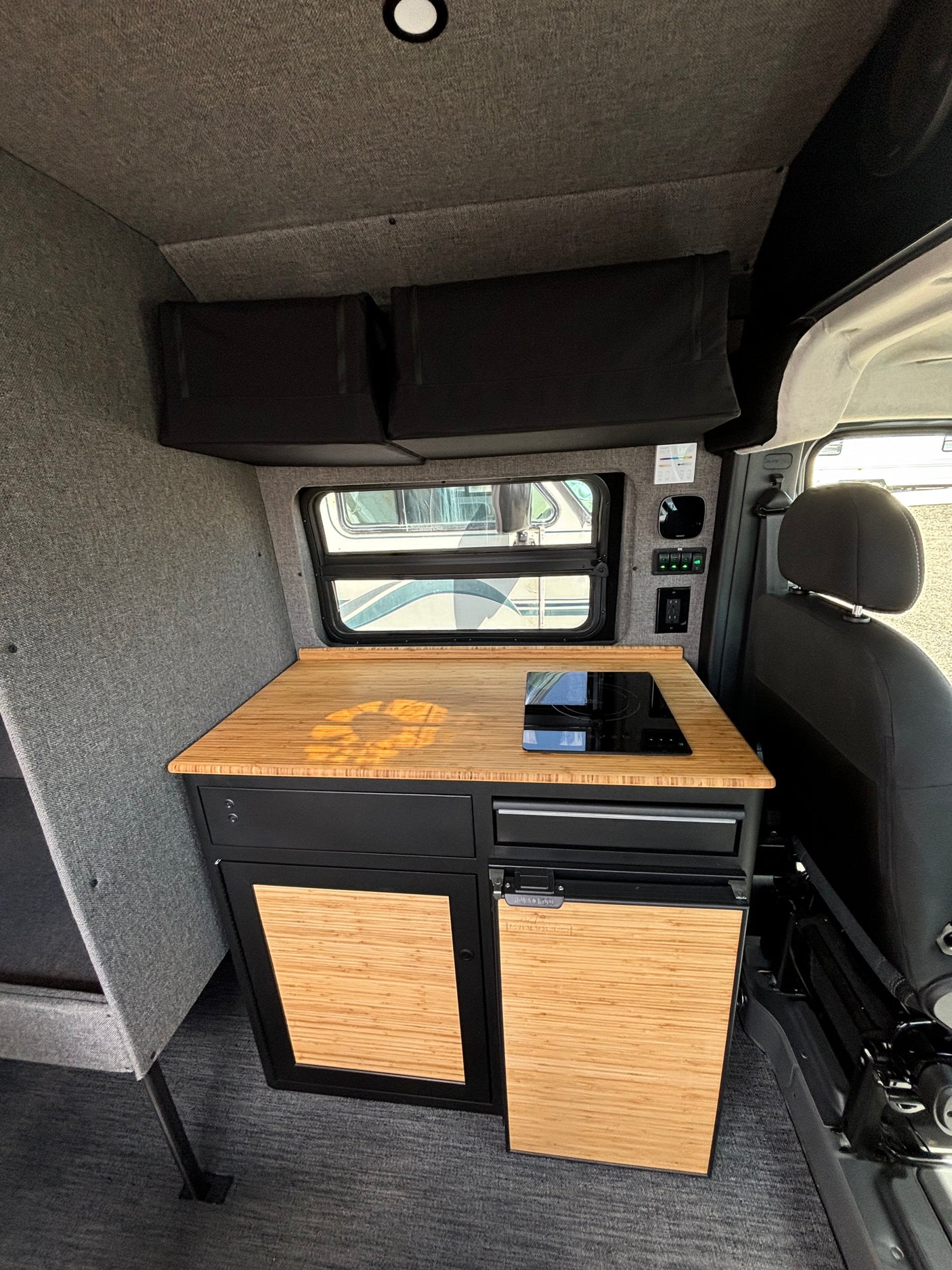 RV rental: Modern camper van interior featuring a bamboo kitchen counter with induction cooktop and compact fridge.