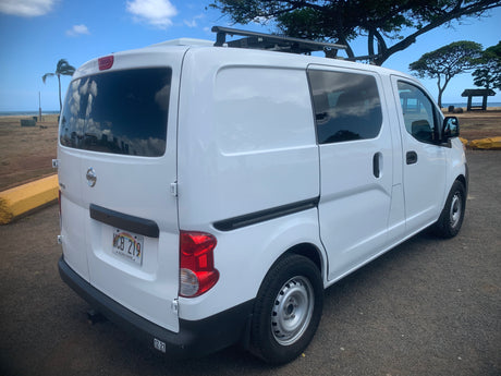 White camper van RV rental with roof rack, parked on a dirt lot next to a Hawaiian beach with palm trees.