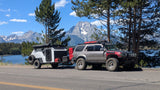 Modified SUV towing an XTR off-road camper by a lake & snow-capped mountains. Consider this RV rental for adventure!