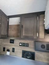RV rental interior: wood-look cabinets (one open), bed, control panels, electrical outlets, and floor vent.