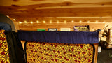 Inside a comfortable RV rental: wooden ceiling, string lights, a shelf of travel books, and a colorful patterned bed area.