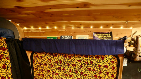 Inside a comfortable RV rental: wooden ceiling, string lights, a shelf of travel books, and a colorful patterned bed area.