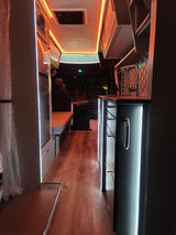 Modern RV rental interior: wood floor, glowing warm lights, sleek kitchen & cozy seating for your adventure.