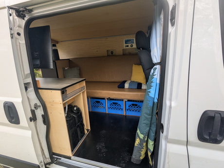 Spacious custom RV rental interior featuring a comfy bench, clever storage with crates, and a full wood build.