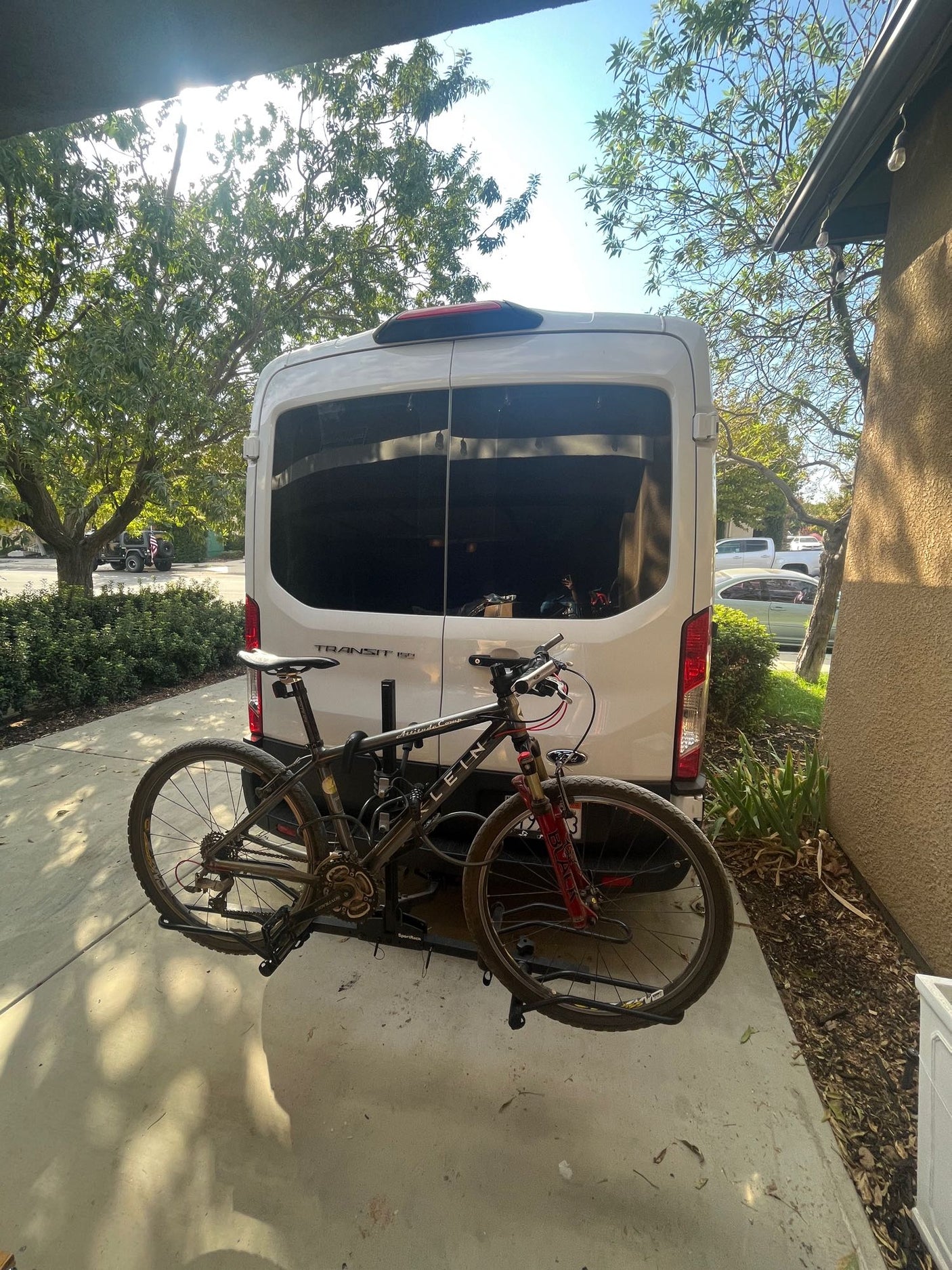 White Ford Transit van with a mountain bike on its rear bike rack, parked on a sunny day. Ideal RV rental for outdoor adventures.