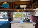 Interior of an rv rental camper van, showing a compact kitchen with sink, utensils, and bed, plus digital displays and an outdoor view.
