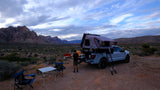 An alternative to an rv rental: Person sets up camp by a pickup with a rooftop tent in the desert mountains.