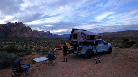 An alternative to an rv rental: Person sets up camp by a pickup with a rooftop tent in the desert mountains.