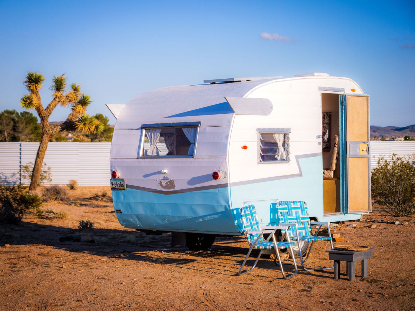 Charming blue & white vintage camper rv rental in the desert. Relax outside with the included chairs and table.