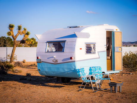 Charming blue & white vintage camper rv rental in the desert. Relax outside with the included chairs and table.