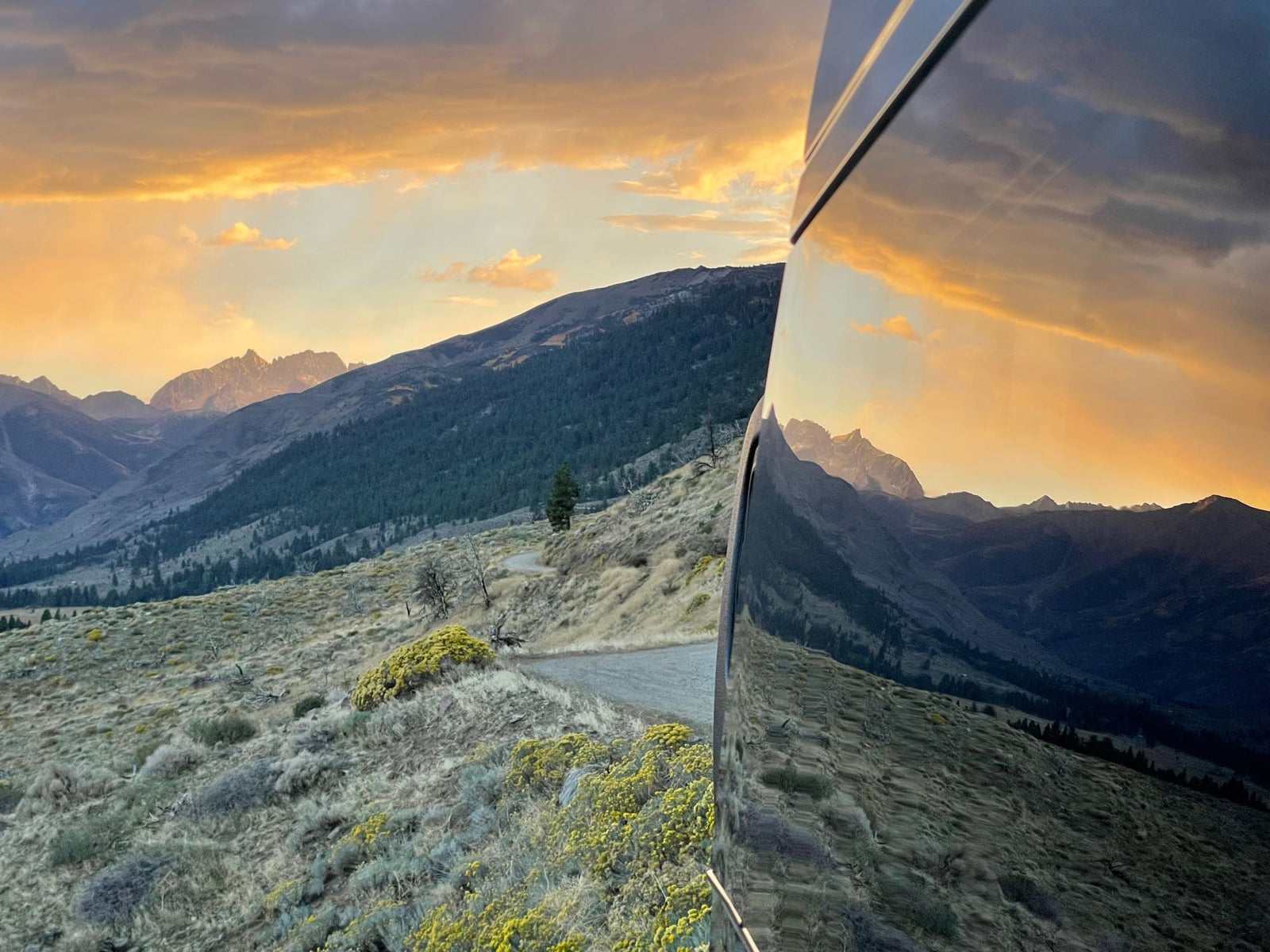Golden sunset over rugged mountains, brilliantly reflected on an RV rental side. Ideal for scenic drives.