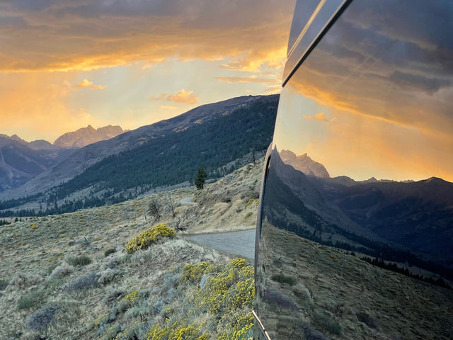 Golden sunset over rugged mountains, brilliantly reflected on an RV rental side. Ideal for scenic drives.