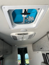 Inside an RV rental: Looking up at the ceiling showing a roof vent with fan and a central air conditioning unit. Overhead storage also visible.