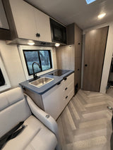 RV rental: Modern kitchen with sink, cooktop, microwave, and light cabinetry. Includes comfy armchair and herringbone floor.