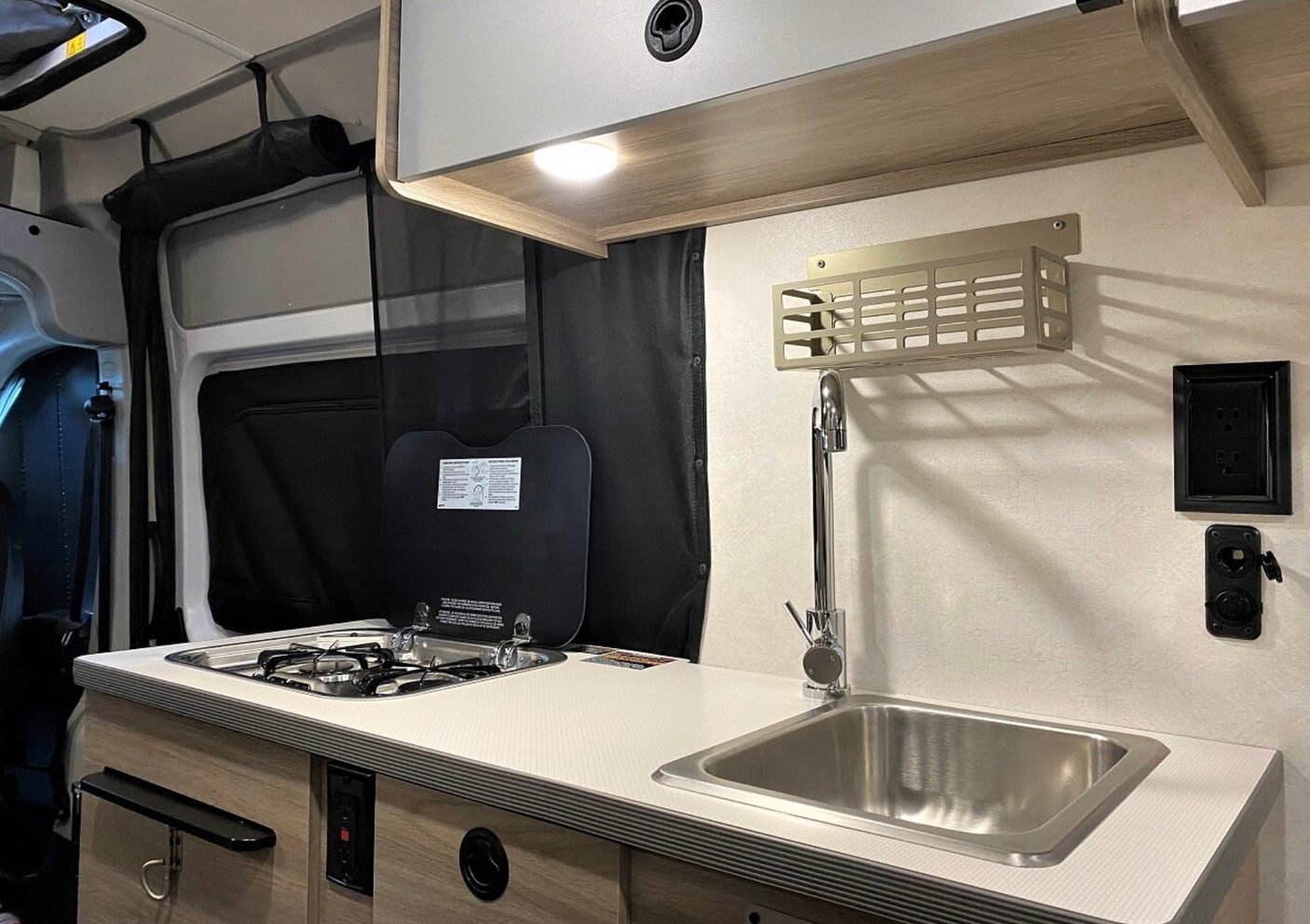Inside an RV rental: a modern, compact kitchen setup featuring a sink, stovetop, and overhead storage.