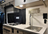 Inside an RV rental: a modern, compact kitchen setup featuring a sink, stovetop, and overhead storage.