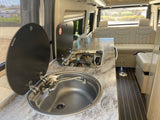 Inside an RV rental: a well-appointed kitchen with sink and two-burner stove, alongside comfortable cream-colored seating.