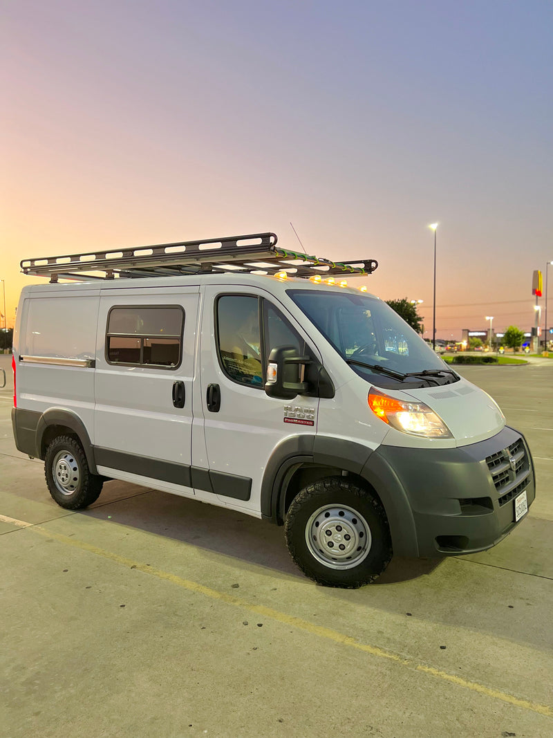 A white Ram ProMaster camper van with a roof rack and rugged tires, parked in a lot at dusk. Perfect for an rv rental. — photo 9