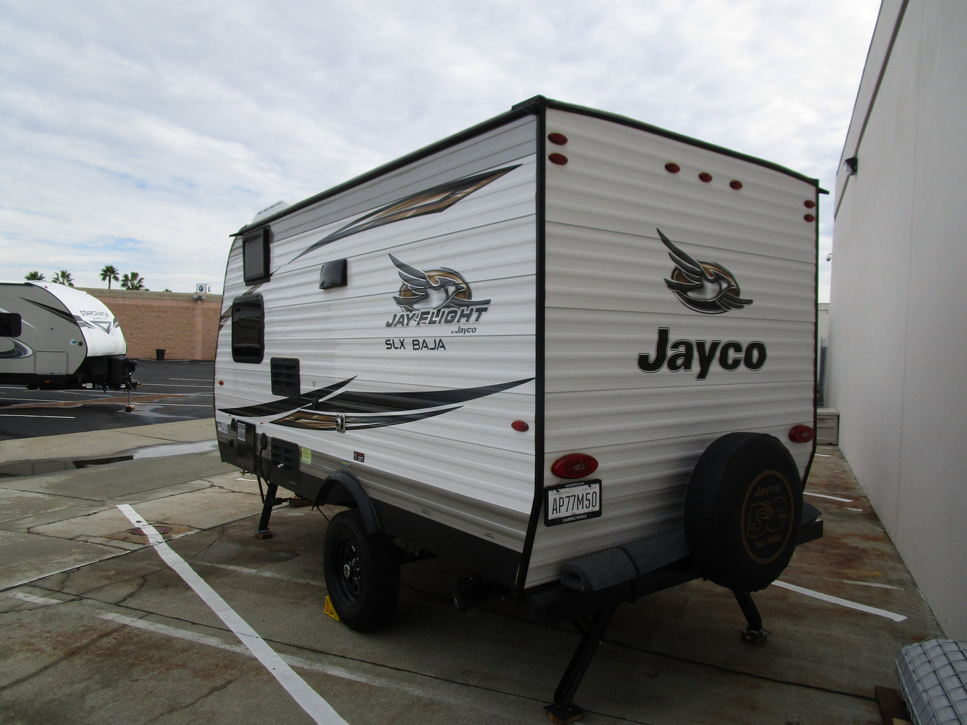 This Jayco Jay Flight SLX BAJA travel trailer, a potential RV rental, is shown parked from its side and rear view.