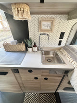 Cozy RV rental kitchenette featuring a sink, herringbone backsplash, and a 'Let's get cozy' sign, perfect for glamping.