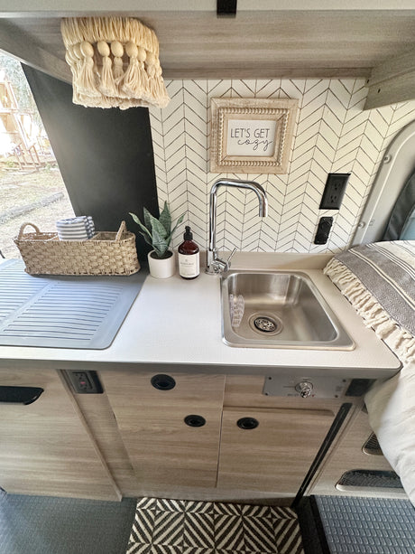 Cozy RV rental kitchenette featuring a sink, herringbone backsplash, and a 'Let's get cozy' sign, perfect for glamping.