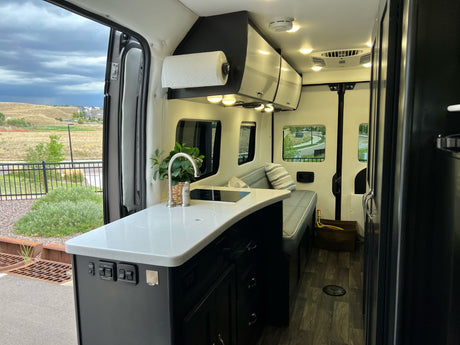 Spacious RV rental interior featuring a modern kitchen area with a sink and stove, and comfortable bench seating.