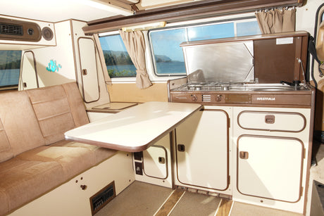 Interior of a retro Westfalia camper van, featuring a cozy seating area, table, and kitchen unit, perfect for an RV rental.