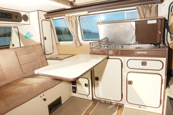 Interior of a retro Westfalia camper van, featuring a cozy seating area, table, and kitchen unit, perfect for an RV rental.
