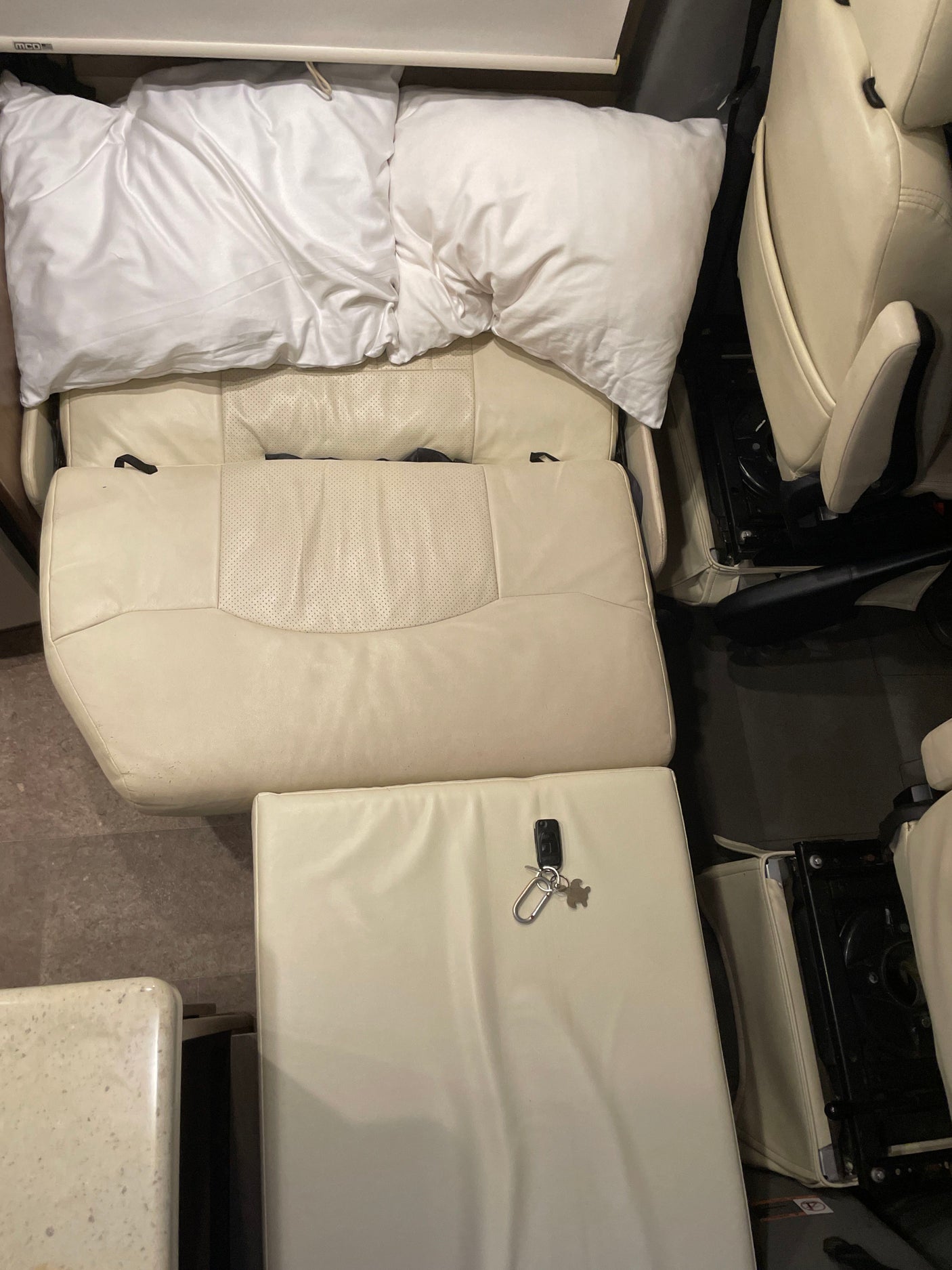 Overhead view of a cozy RV rental interior: cream leather seats converted to a bed with pillows. Keys on a cushion.