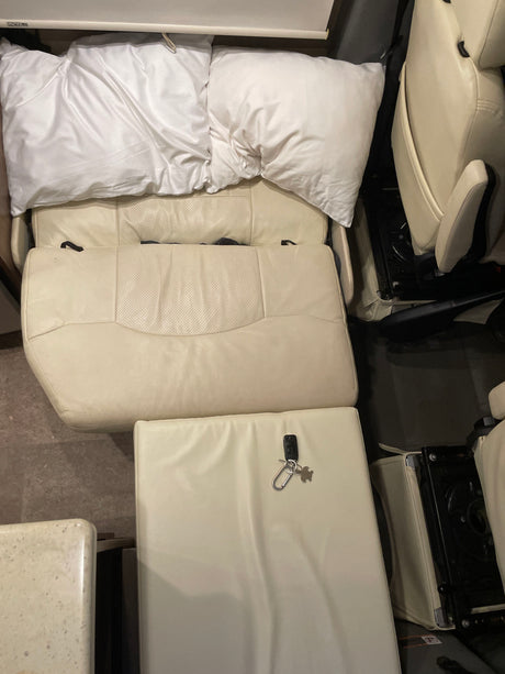 Overhead view of a cozy RV rental interior: cream leather seats converted to a bed with pillows. Keys on a cushion.